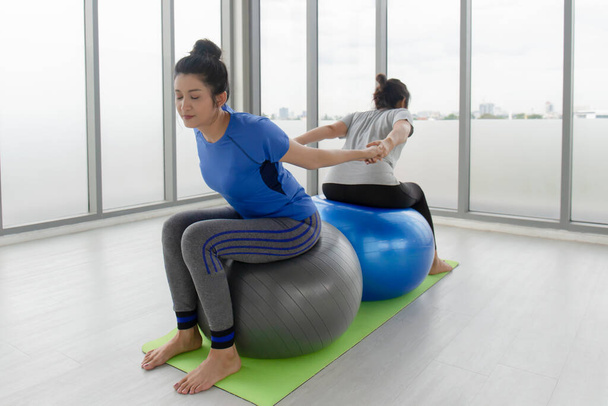 Two middle-aged Asian women doing yoga sitting on a rubber ball in the gym. - Valokuva, kuva