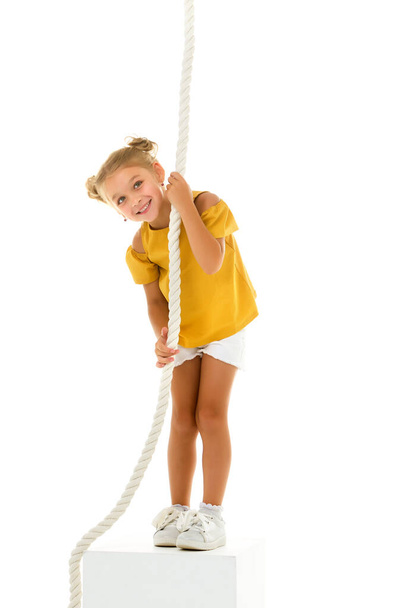 Ένα κοριτσάκι κρατιέται από το σκοινί με τα χέρια της, κρεμασμένο πάνω του.. - Φωτογραφία, εικόνα