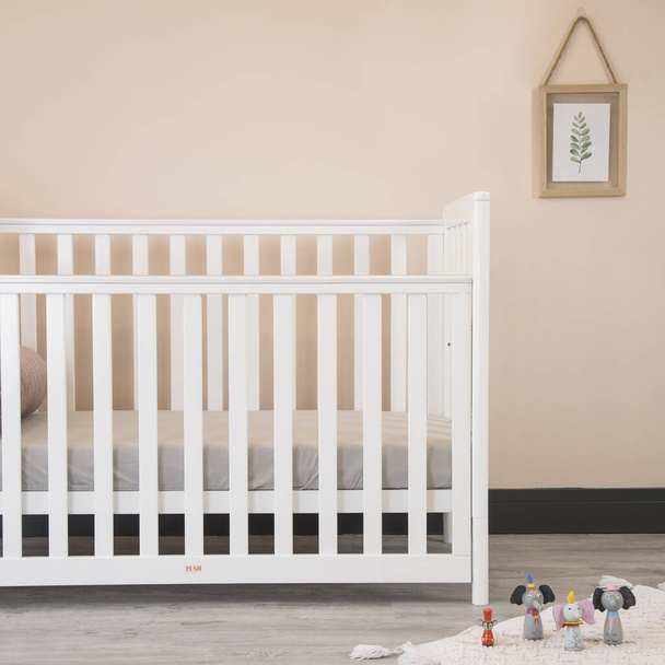 A modern baby room interior with a cozy classic crib and miniature toys placed on a soft carpet - Фото, изображение
