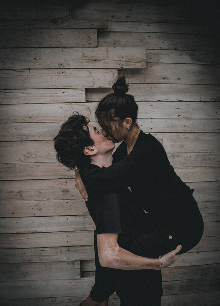 a young boy and girl passionately kissing each on the wooden wall background - Foto, imagen