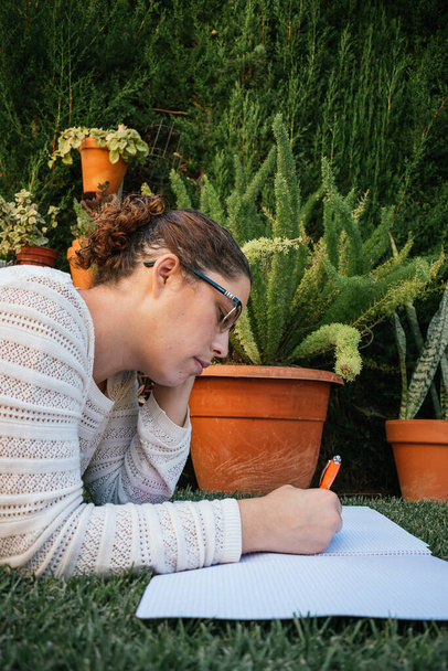 Caucasian woman doing homework on a garden lawn - Foto, Imagen