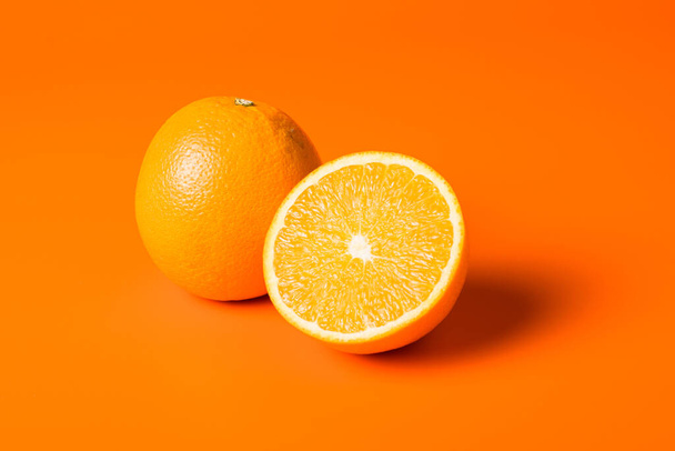A closeup shot of a ripe and a half-cut orange on orange background - Foto, Imagem
