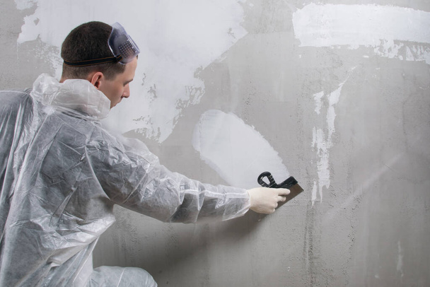 a worker in a protective uniform applies a finishing white putty to a concrete wall - Φωτογραφία, εικόνα