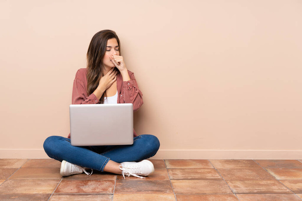 Teenager student girl sitting on the floor with a laptop is suffering with cough and feeling bad - Foto, imagen