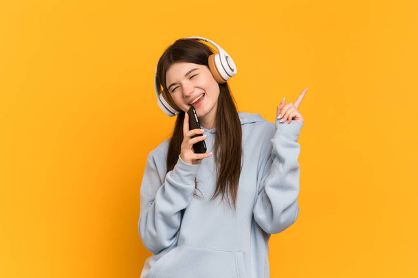 Nuori ukrainalainen tyttö eristetty keltaisella taustalla kuuntelee musiikkia mobiili ja laulaa - Valokuva, kuva