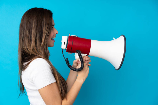 Teenager girl over isolated blue background shouting through a megaphone - Foto, immagini