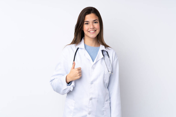 Chica adolescente sobre fondo blanco aislado con una bata de médico y con el pulgar hacia arriba - Foto, imagen