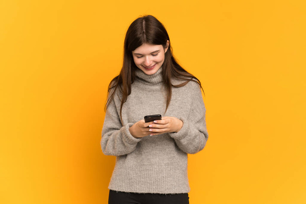 Young Ukrainian girl isolated on yellow background sending a message with the mobile - Fotó, kép