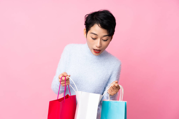 Joven asiática chica sobre aislado rosa fondo sosteniendo bolsas de compras y mirando dentro de ella - Foto, imagen