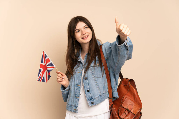 Young Ukrainian girl holding an United Kingdom flag isolated on beige background giving a thumbs up gesture - Photo, Image