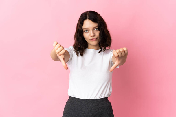 Teenager Ukrainian girl isolated on pink background showing thumb down with two hands - Photo, Image