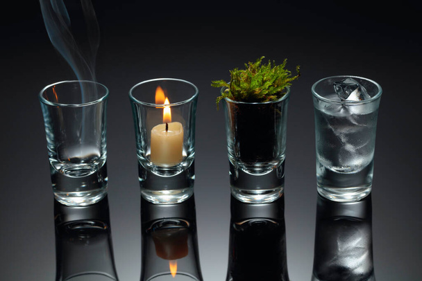 Vier Elemente der Natur - Luft, Feuer, Erde, Wasser. Vier Elemente Konzept in Gläsern auf schwarzem reflektierendem Hintergrund. - Foto, Bild