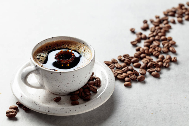 Black coffee and coffee beans on a white table. A drop of coffee fall in a cup. Copy space. - Valokuva, kuva