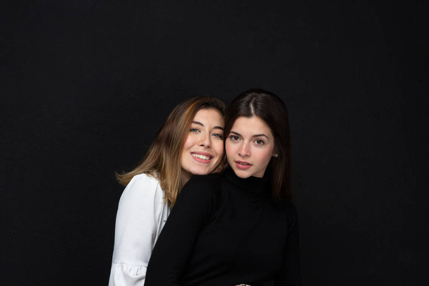 Portrait of two happy women friends with loving gestures laughing on a black background - Concept of friendship - Foto, immagini