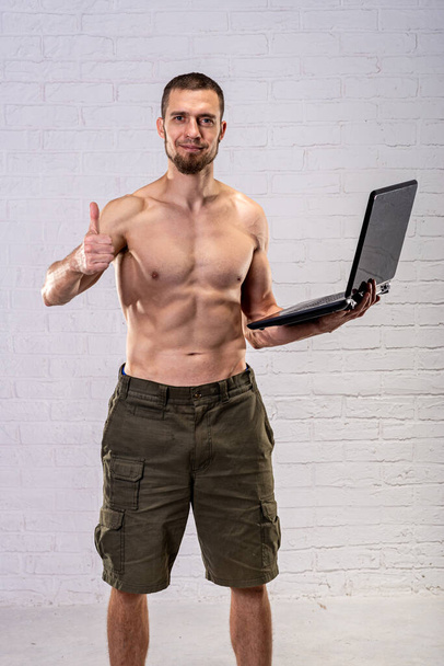 A man with a naked torso holds a laptop and shows the ok sign. Remote training. Trainer. - Fotografie, Obrázek