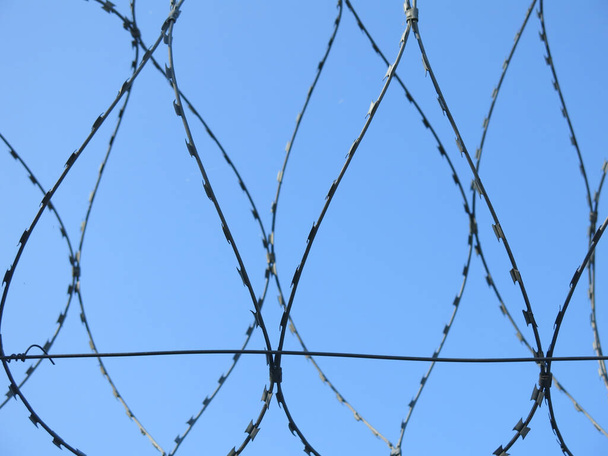 prikkeldraad tegen een heldere blauwe lucht, als een gevangenis - Foto, afbeelding
