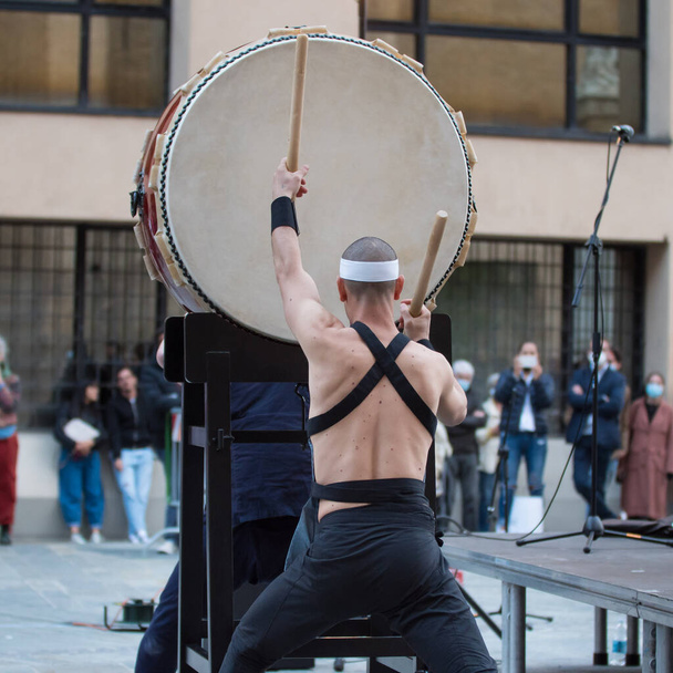 Hombre con diadema tocando el tambor vertical de la tradición musical japonesa durante un evento público al aire libre. - Foto, imagen