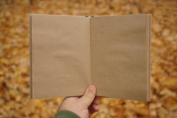 male hand holding open book on  autumn park background. Craft paper - Foto, Imagen