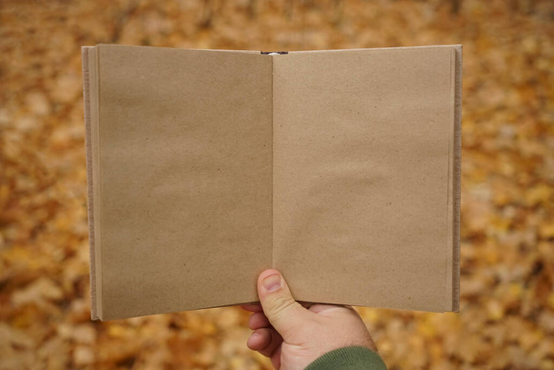 man holding open book on  autumn park background. Craft paper - Foto, imagen