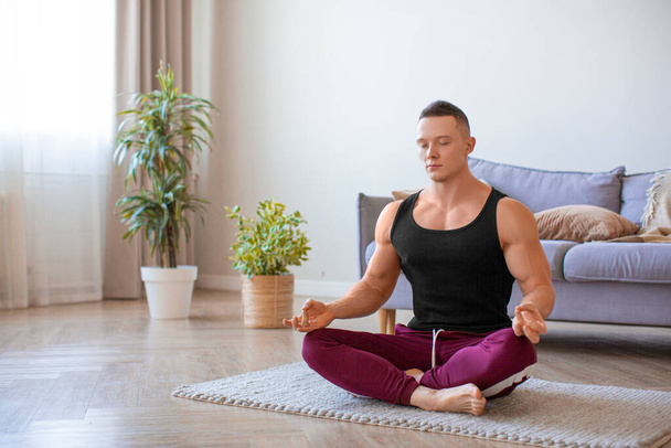 Young fit man practicing yoga at home. Meditation and calmness. - Photo, Image