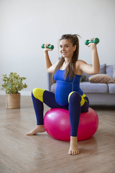 Vertical photo of a smiling pregnant woman at home. Yoga of pilates workout with fit ball. - Foto, Imagem