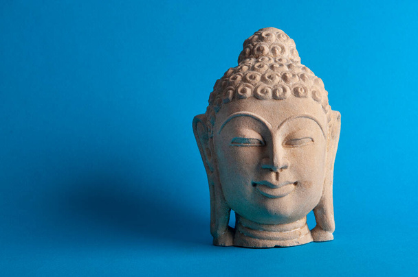 Sculpture of Buddha face on a blue background - Foto, afbeelding