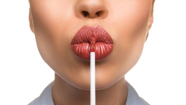 Vrouw die een lipgloss op haar lippen aanbrengt op een witte achtergrond. Zoenen. Sluiten.. - Foto, afbeelding