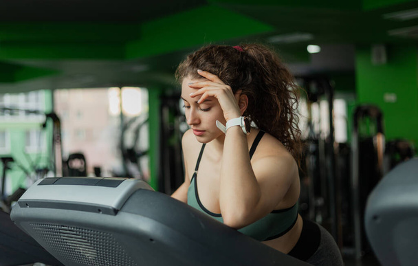 Tired Young fit woman in sportswear on treadmill in the gym. The concept of a healthy lifestyle, warming up, fitness. - 写真・画像