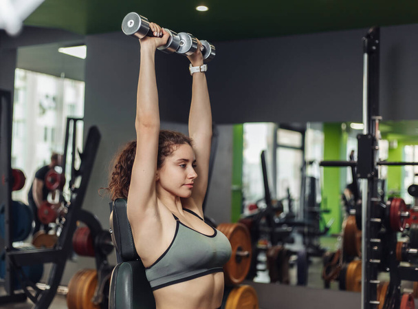 Jeune femme en forme faisant des exercices de presse de banc d'haltère dans la salle de gym. Concept de mode de vie sain. Entraînement poids gratuit - Photo, image