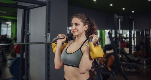Spor salonunda kettlebell egzersizi yapan atletik fit genç bir kadın. Serbest ağırlık, fonksiyonel eğitim - Fotoğraf, Görsel