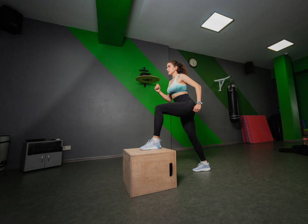 Genç, formda bir kadın spor dersinde tahta bir kutuya basıyor. Fonksiyonel eğitim, egzersiz. - Fotoğraf, Görsel