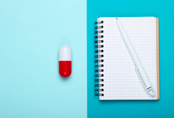 Composizione della medicina laica piatta. Capsula pillola, quaderno su sfondo blu pastello. Vista dall'alto - Foto, immagini