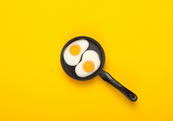 Sartén miniatura de juguete con huevos fritos sobre fondo amarillo. Vista superior. Concepto de comida minimalista, desayuno. Captura de estudio - Foto, imagen