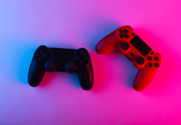 Δύο Gamepads με νέον μπλε-ροζ φως. Έννοια παιχνιδιού. - Φωτογραφία, εικόνα