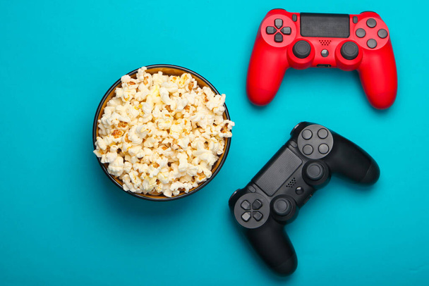 Two gamepads and a bowl of popcorn on blue background. Gaming, leisure and entertainment concept. Top view - Photo, Image