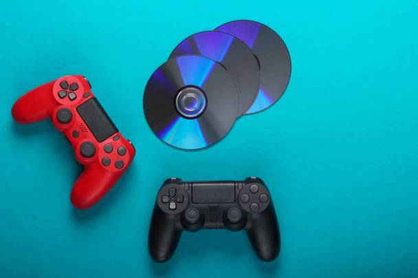 Два геймпада и компакт-диски на синем фоне. Игры, развлекательная концепция. Вид сверху - Фото, изображение