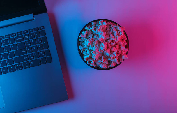 Portatile e ciotola di popcorn con luce al neon rosa blu. Concetto di svago e intrattenimento. Vista dall'alto - Foto, immagini