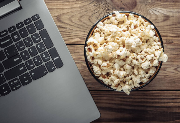 Laptop, bowl of popcorn on wooden table. Leisure and entertainment concept. Top view - Photo, image