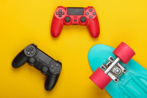Gamepads with cruiser board on a yellow background. Childhood concept, summer fun, entertainment. Top view. Flat lay - Photo, Image