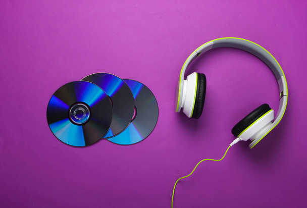 Stylish wired stereo headphones and cd discs on purple background. Music lover. Retro 90s. Top view. - Photo, Image