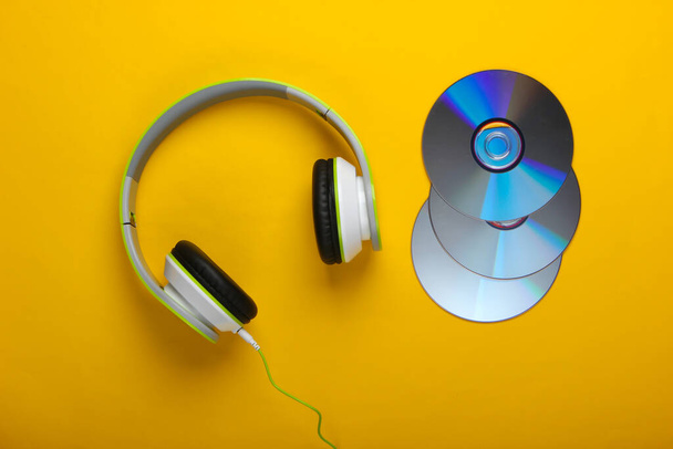 Stylish wired stereo headphones and cd discs on yellow background. Music lover. Retro 90s. Top view. - Photo, Image