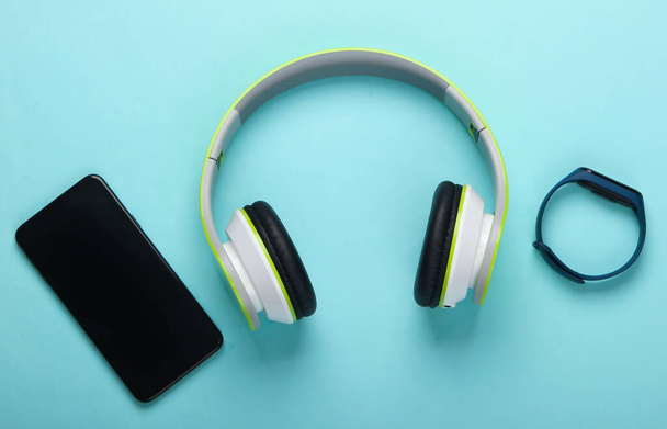Plochá kompozice moderních přístrojů. Bezdrátová sluchátka, chytrý náramek, chytrý telefon na modrém pozadí. Tisícileté věci. Horní pohled - Fotografie, Obrázek