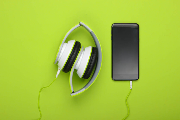 Casque stéréo pliant portable avec smartphone sur fond vert. Amoureux de musique. Des gadgets modernes. Vue de dessus. Minimalisme - Photo, image