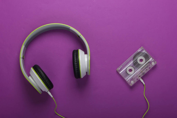 Elegantes auriculares estéreo con cable con casete de audio sobre fondo púrpura. Amante de la música. Retro 80. Vista superior. - Foto, imagen