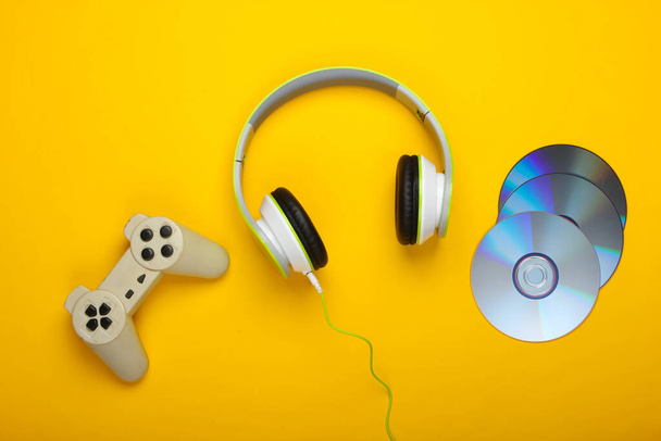 Stereo headphones with gamepad, cd discs on yellow background. Gaming, leisure and entertainment concept. Top view. - Photo, Image