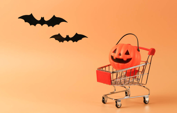 Front view of  Halloween pumpkin on shopping cart  on orange background decorated with black paper bats.copy space. Halloween holiday concept. - Fotoğraf, Görsel