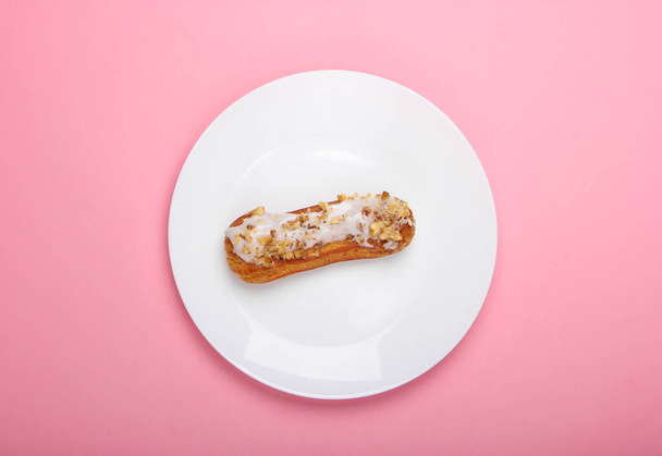 Eclair on the plate. Pink pastel background. Dessert. Top view, minimalism - Фото, зображення