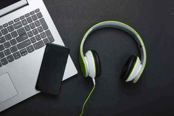 Laptop sztereó fejhallgatóval és okostelefonnal fekete háttérrel. Lapos kompozíció. Modern kütyü. Felülnézet - Fotó, kép