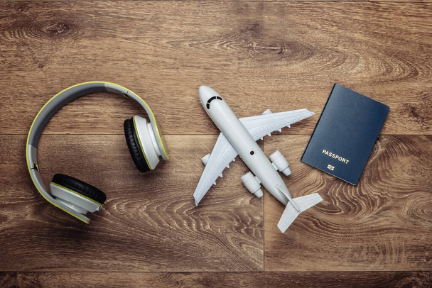 Travel concept. Headphones, airplane figurine, passport on wooden floor. Flight voyage, trip, journey design. Flat lay composition. Top view - Photo, Image
