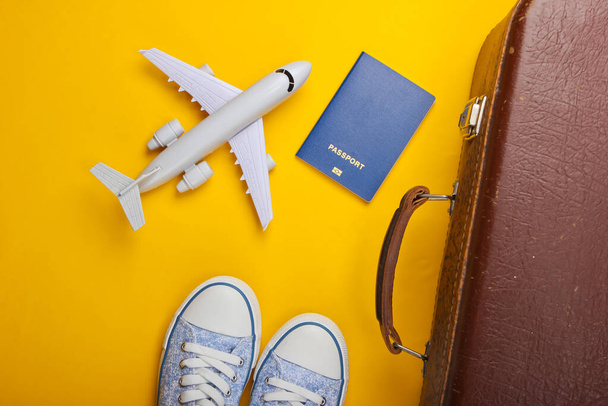 Travel concept. Old luggage, airplane figurine, passport, sneakers on yellow background. Flight voyage, trip, journey. Flat lay composition. Top view - Photo, Image